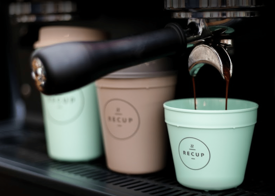 Branded Recup coffee cups are filled with coffee at a coffee machine.